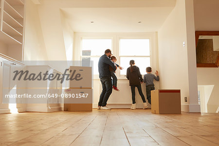 Mid adult man and three children looking from window of new home