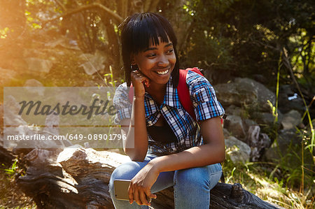 Young woman in forest, sitting on fallen tree, holding smartphone, Cape Town, South Africa