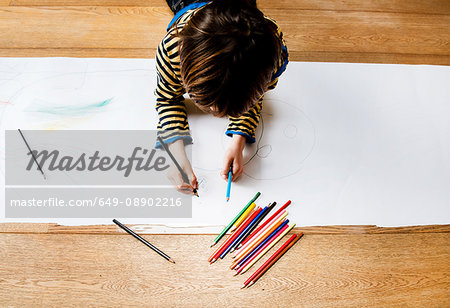 Overhead view of boy lying on floor drawing on long paper