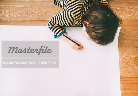 Overhead view of boy drawing on large paper on floor