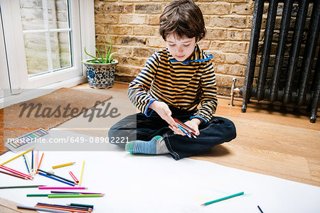Boy sitting on floor drawing on long paper