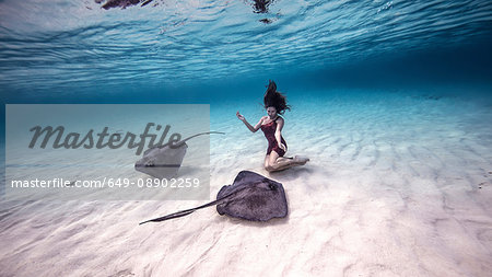 Female free diver kneeling near stingrays on seabed
