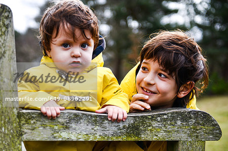 Portrait of baby boy and big brother in yellow anoraks on park bench