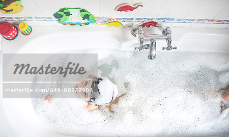 Boy sitting in bath, bubbles on head, smiling, overhead view
