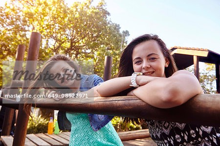 Portrait of two female friends sitting on climbing frame at park