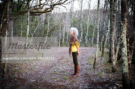 Mature woman standing in woodland looking