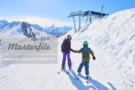 Rear view of girl and brother holding hands on ski slope, Gstaad, Switzerland