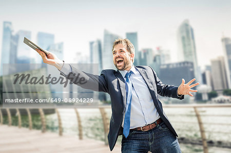 Happy businessman holding out digital tablet on city waterfront