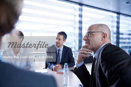 Over shoulder view of businesswoman and men listening at office meeting