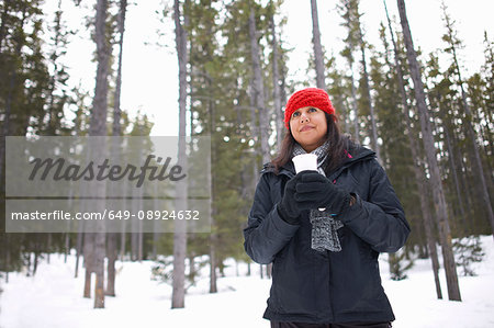 Woman by snow covered forest holding hot drink, Banff, Canada