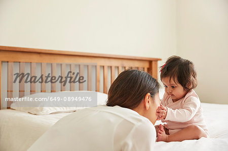 Baby girl sitting up on bed touching mother's face
