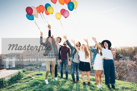 Portrait of group of friends, standing on roof, holding helium balloons