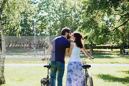 Rear view of couple with bicycles kissing in park, Arezzo, Tuscany, Italy