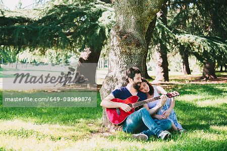 Couple sitting in park playing guitar, Arezzo, Tuscany, Italy