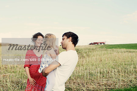 Pregnant couple in wheat field with toddler daughter