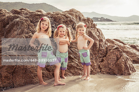 Portrait of three young sisters on beside rock on beach, smiling