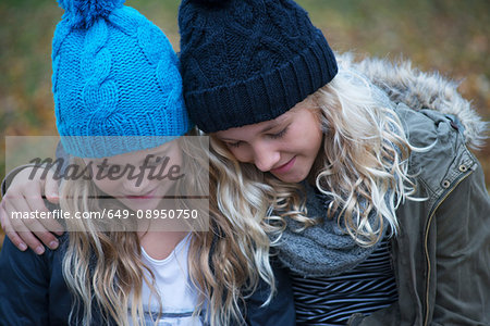 Blond haired sisters wearing knit hats looking down in garden