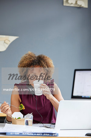 Female designer having working lunch and looking at laptop at desk