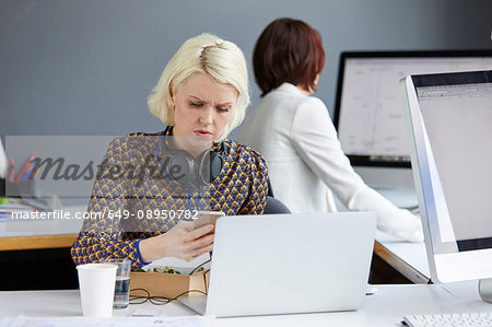 Female designer looking at smartphone during working lunch at office desk