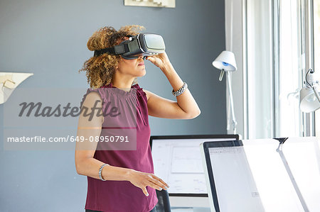 Female architect looking through virtual reality headset at office desk