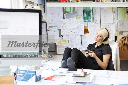 Female designer with feet up at desk listening to headphone music