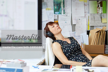 Female designer at office desk listening to headphone music  with eyes closed