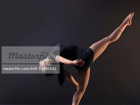 Low key shot of young female dancer bending backwards whilst standing on one leg