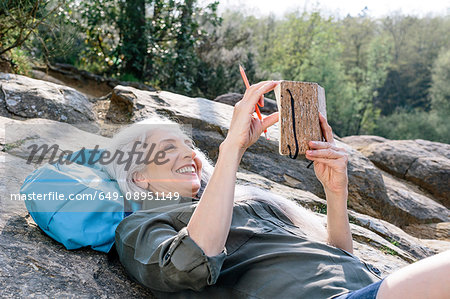 Mature female backpacker reclining on rock in forest, Scandicci, Tuscany, Italy Mature female backpacker reclining on rock in forest, Scandicci, Tuscany, Italy