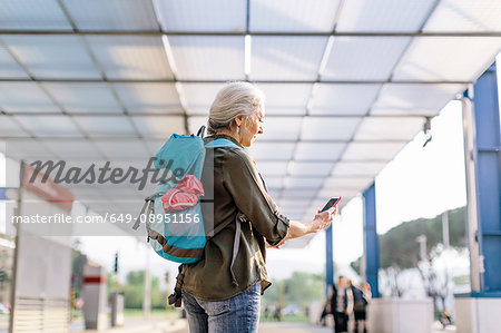 Mature female backpacker looking at smartphone in bus station, Scandicci, Tuscany, Italy