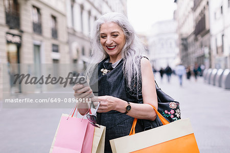 Stylish mature female shopper looking at smartphone on street, Florence, Italy