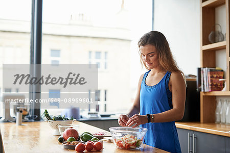 Young woman at kitchen table preparing salad bowl