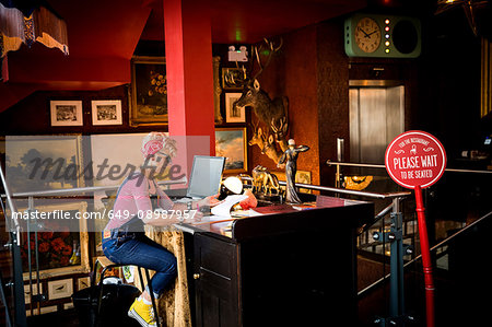 Quirky woman working at high counter at bar and restaurant, Bournemouth, England
