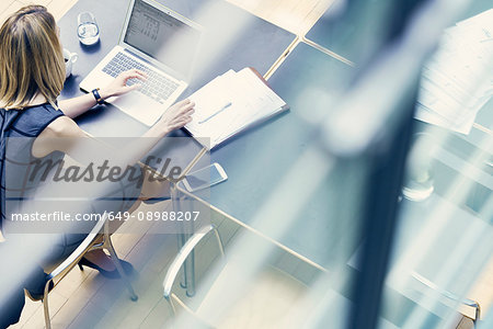 High angle window view of young businesswoman typing on laptop at office desk