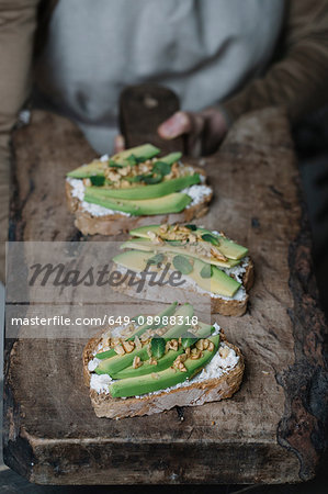 Woman holding chopping board, with ricotta, avocado and walnut bruschetta on top, close-up