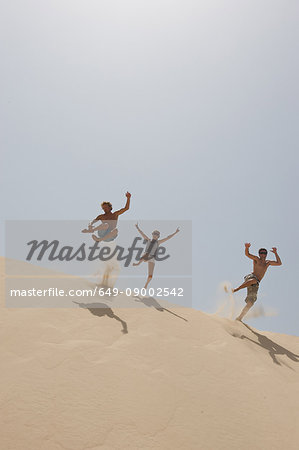 Friends jumping over a big sand dune