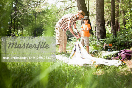 Father and son pitching tent in forest