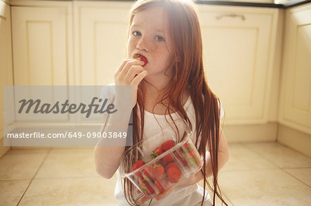 Girl eating strawberry on kitchen floor