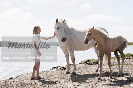 Girl petting horses on sandy beach