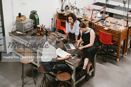 High angle view of three female jewellers having discussion at workbench meeting