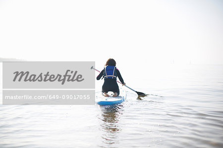 Rear view of female paddleboarder paddling out on misty sea
