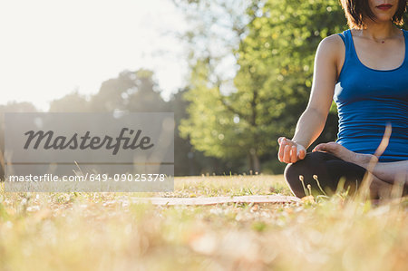 Mature woman in park, sitting in yoga position, low angle view