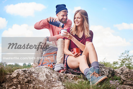 Couple hiking, sitting on rocks pouring drink from flask into enamel mug, Krakow, Malopolskie, Poland, Europe
