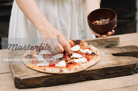 Woman putting olives on homemade pizza, mid section