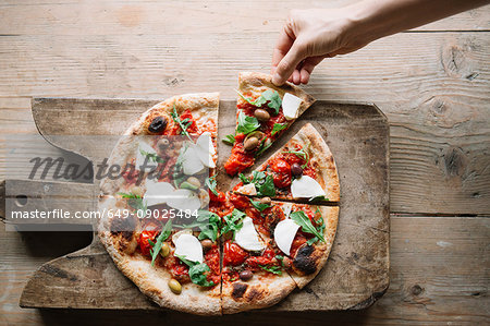 Woman taking pizza slice from pizza on chopping board, overhead view