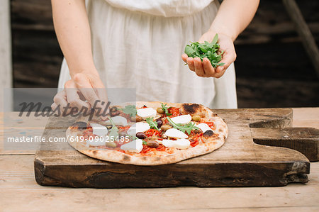 Woman putting herbs on home-made pizza, mid section
