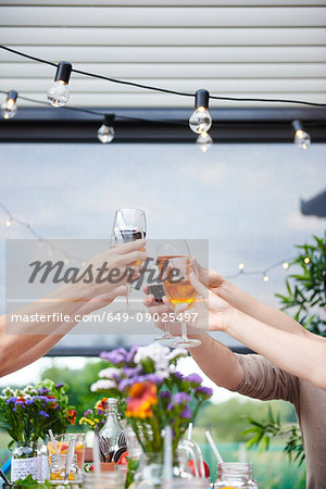 Hands of men and women raising a family wine toast at patio table