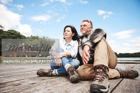 Mature couple relaxing on jetty beside lake