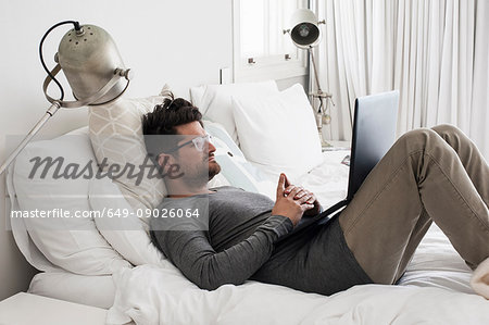 Mid adult man lying on bed, using laptop