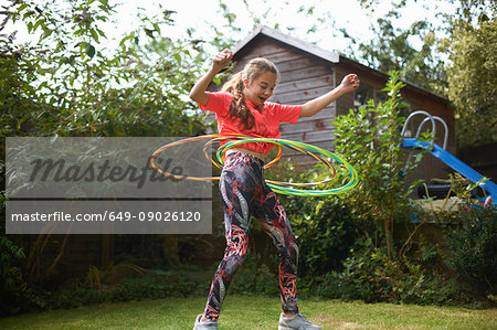 Teenage girl hula hooping with four plastic hoops in garden