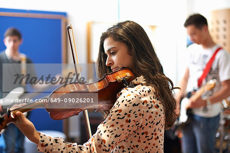 Young female college student playing violin in recording studio